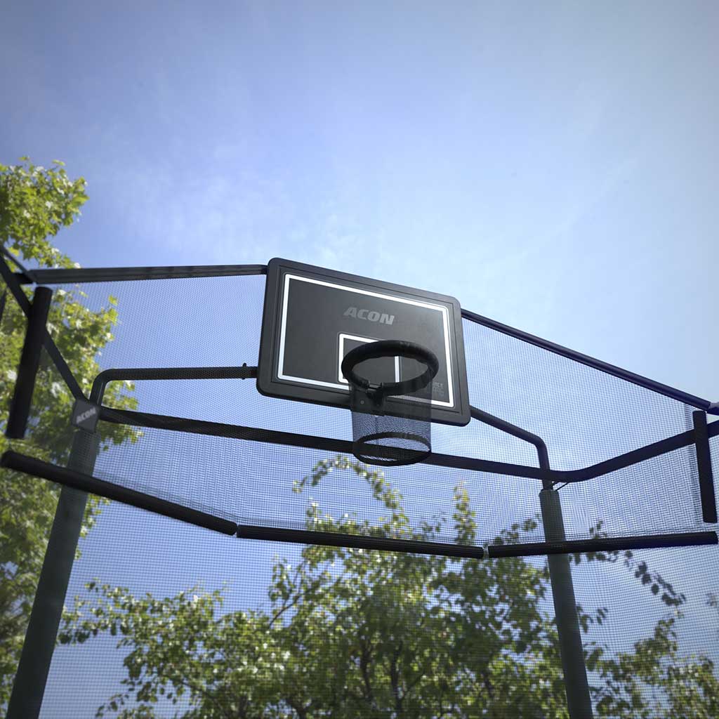 Utomhusbild av Acon basketkorg för rektangulär studsmatta med bollfångarnät sedd underifrån, som visar blå himmel och omgivande träd.