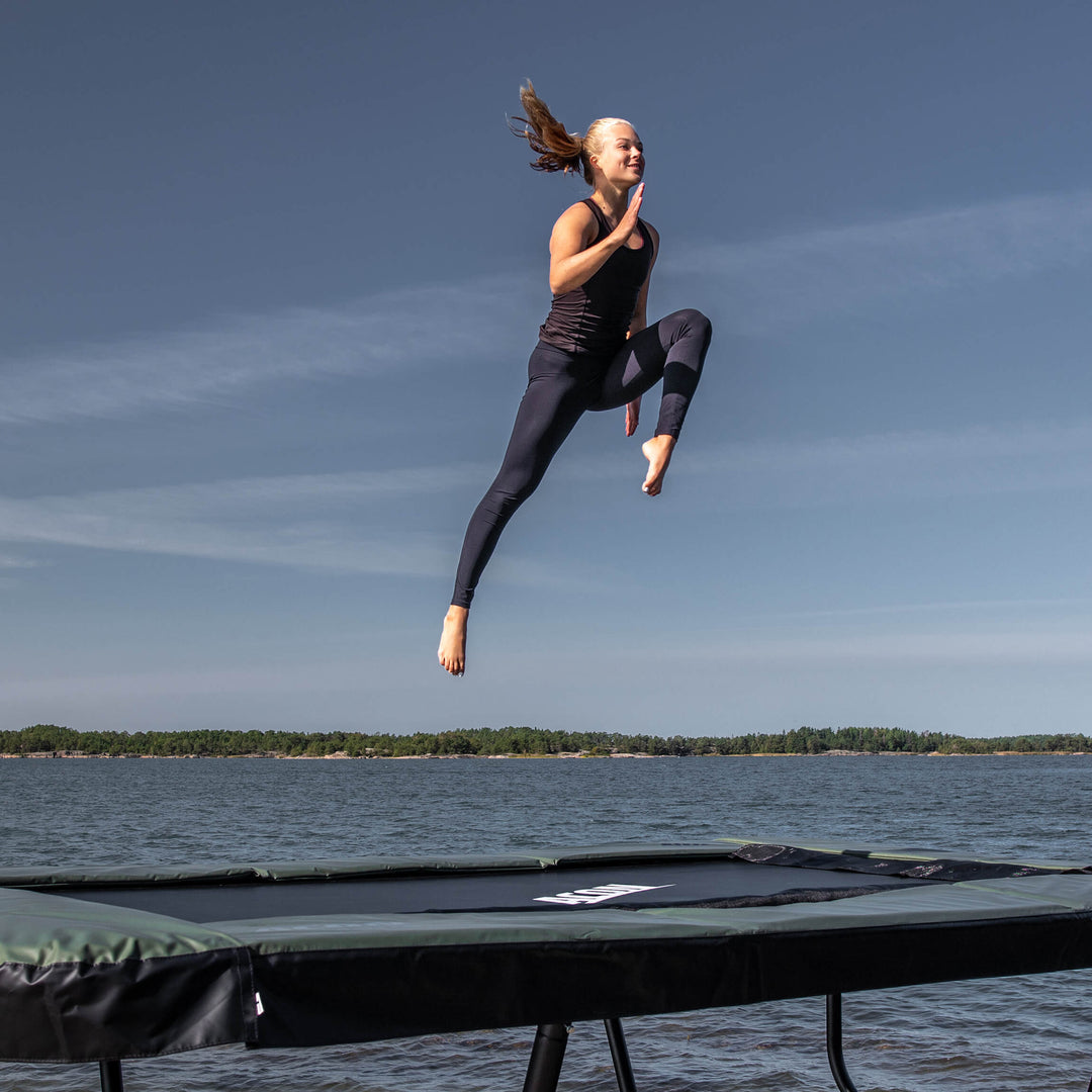 En gymnast hoppar på en Acon 13 Sport HD studsmatta i ett skärgårdslandskap.